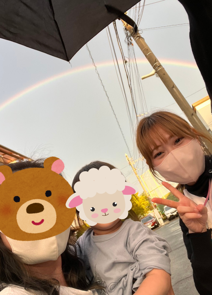 虹を背景に利用者の家族と写真を撮る看護師
